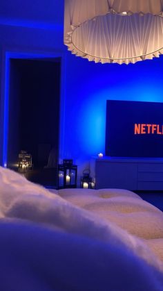 a room with blue lighting and white sheets on the bed, next to a television that reads netflix