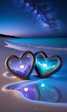 two heart shaped candles sitting on top of a sandy beach under a night sky filled with stars