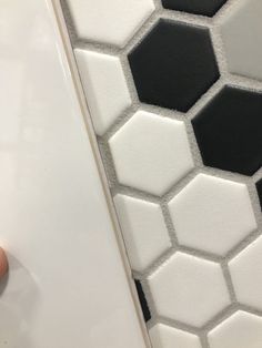 a person's hand on the floor next to a tile wall with black and white hexagonal tiles