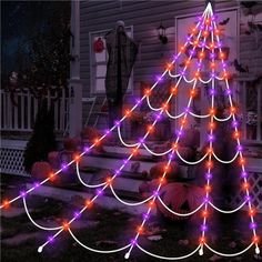 a lighted christmas tree in front of a house with pumpkins on the ground and other decorations around it