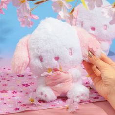 a person holding a small stuffed animal in front of pink and white flowers on a table