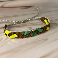 a yellow and green beaded bracelet on a wooden table with a silver string attached to it