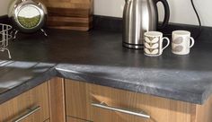 a kitchen counter with two coffee mugs and a kettle on the counter next to it