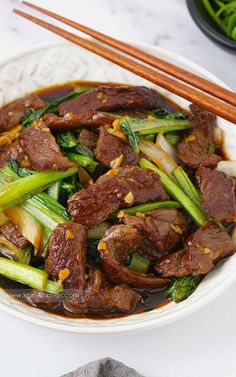 beef and vegetable stir fry with chopsticks in a white bowl on a table