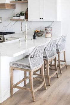 three chairs sitting at the end of a kitchen island with marble counter tops and white cabinets