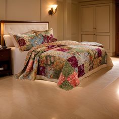 a bedroom with a large bed covered in colorful quilts and pillows next to a night stand