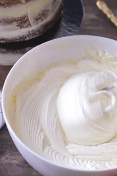 a bowl filled with white frosting next to a cake on top of a table