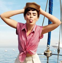 a woman wearing a hat standing on the deck of a boat with her hands behind her head