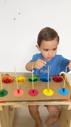 a young boy sitting at a table with paint and toothpicks in front of him