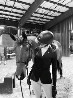 a woman standing next to a horse wearing a helmet on it's head in an indoor arena