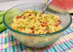 a bowl filled with macaroni salad next to a watermelon slice on a table