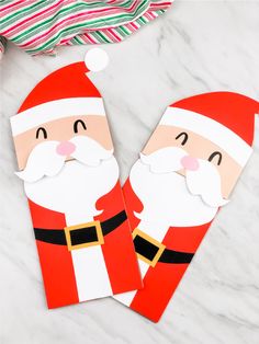 two paper santa clauss sitting on top of a white counter next to a red and green striped towel