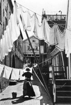 an old black and white photo of a woman sitting on the sidewalk in front of some laundry lines