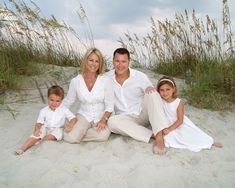 a man, woman and two children sitting on the sand at the beach with sea oats in the background