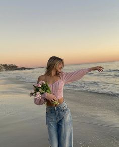 a woman is standing on the beach with flowers in her hand and pointing at the water