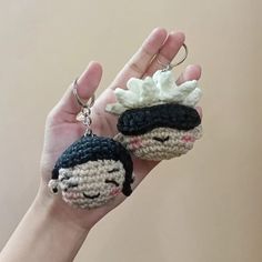 a hand holding two crocheted keychains in the shape of dolls