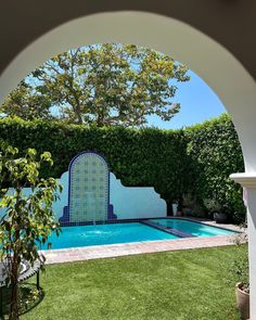 an outdoor swimming pool surrounded by greenery and trees in the back yard, viewed through an archway