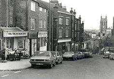 an old black and white photo of cars parked on the side of the road in front of buildings