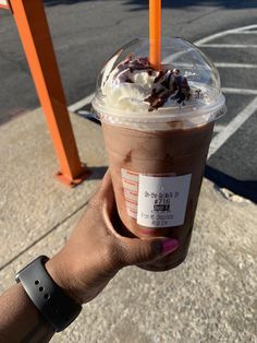 a person holding up a drink with whipped cream and chocolate toppings on it in front of a parking lot