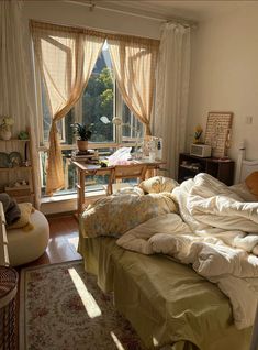 an unmade bed sitting in front of a window next to a desk and chair