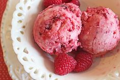 two scoops of ice cream with raspberries in a white bowl