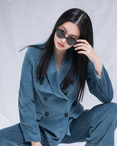 a woman sitting on the ground with her hands in her pockets and sunglasses over her eyes