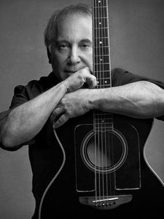 a black and white photo of a man leaning on a guitar with his arms crossed