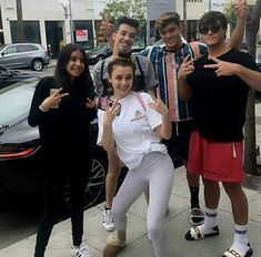 four people posing for a photo on the sidewalk with one person holding up two fingers