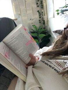 a woman laying in bed reading a book with glasses on her head and looking at the camera