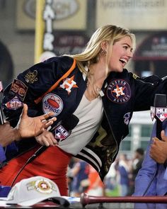 two women are dancing together in front of an audience at a sporting event and one woman is wearing a jacket with patches on it