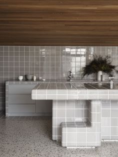 a kitchen with white and grey tiles on the walls, counter tops and sink area