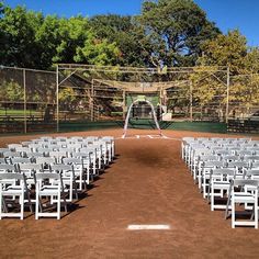 rows of white chairs sitting on top of a dirt field next to a tennis court