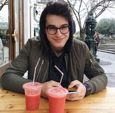 a man sitting at a table with two drinks in front of him and looking at his cell phone