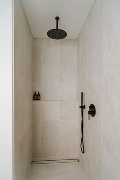 a walk in shower sitting next to a white tiled wall with black faucet