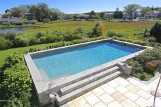 an empty swimming pool in the middle of a lush green yard with steps leading up to it