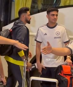 two men are talking to each other while standing in front of a bus with luggage