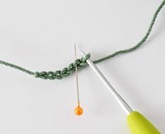 two knitting needles and an orange ball on a green string, with one hook hooked up to the thread