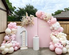 a pink and white wedding arch with balloons on the wall, flowers and candles in vases