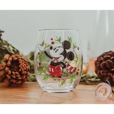 a mickey mouse wine glass sitting on top of a wooden table next to pine cones