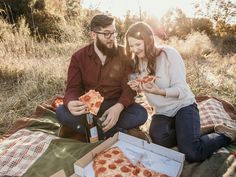 a man and woman sitting on a blanket eating pizza