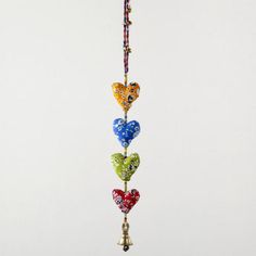 a multicolored heart mobile hanging from a string with bells on it's end