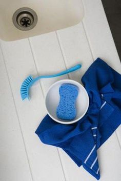 a bowl with a blue scrubber next to a sink and a blue towel on the floor