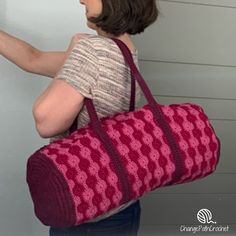 a woman carrying a pink crocheted bag in front of a white wall and door