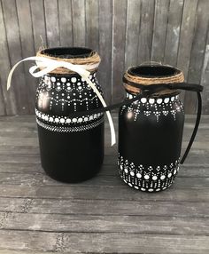 two black jars with white designs and twine tied to each other on a wooden table