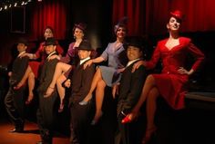 a group of people dressed in costume posing for a photo on stage with red curtains behind them