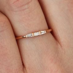 a woman's hand with a gold band and two small white stones on it