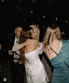 two women hugging each other in a group at a party with people standing around them