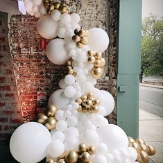 white and gold balloons are hanging from the side of a building in front of a brick wall