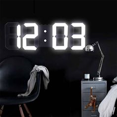 an alarm clock sitting on top of a night stand next to a chair and lamp