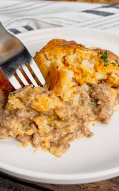 a white plate topped with meat and cheese covered casserole next to a fork